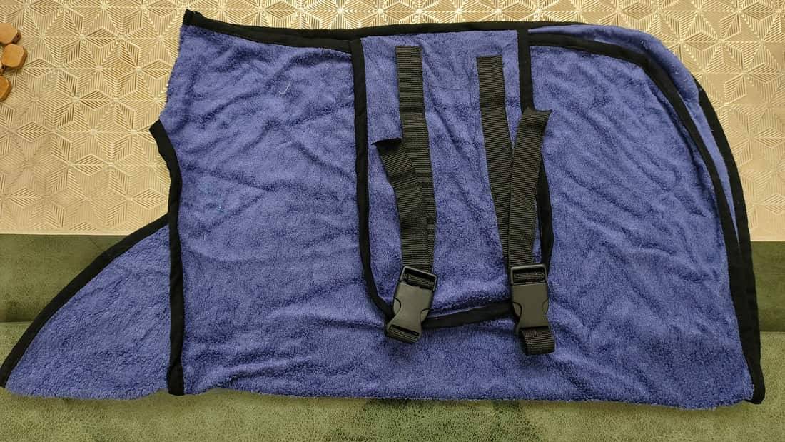 Blue Furrybae dog bathrobe laid flat, showing the terry wrap, black trim and two adjustable buckle straps