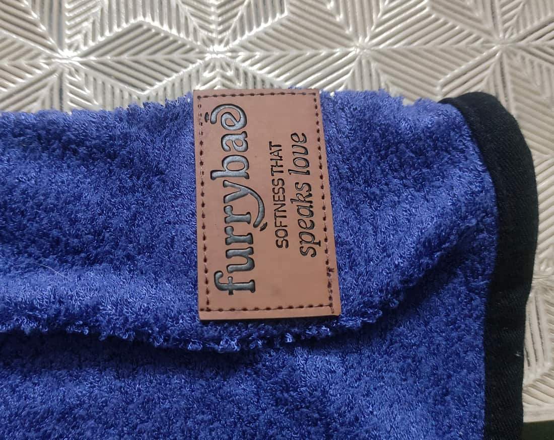 Close-up of the Furrybae leather label on the blue bamboo cotton terry, reading Softness that speaks love